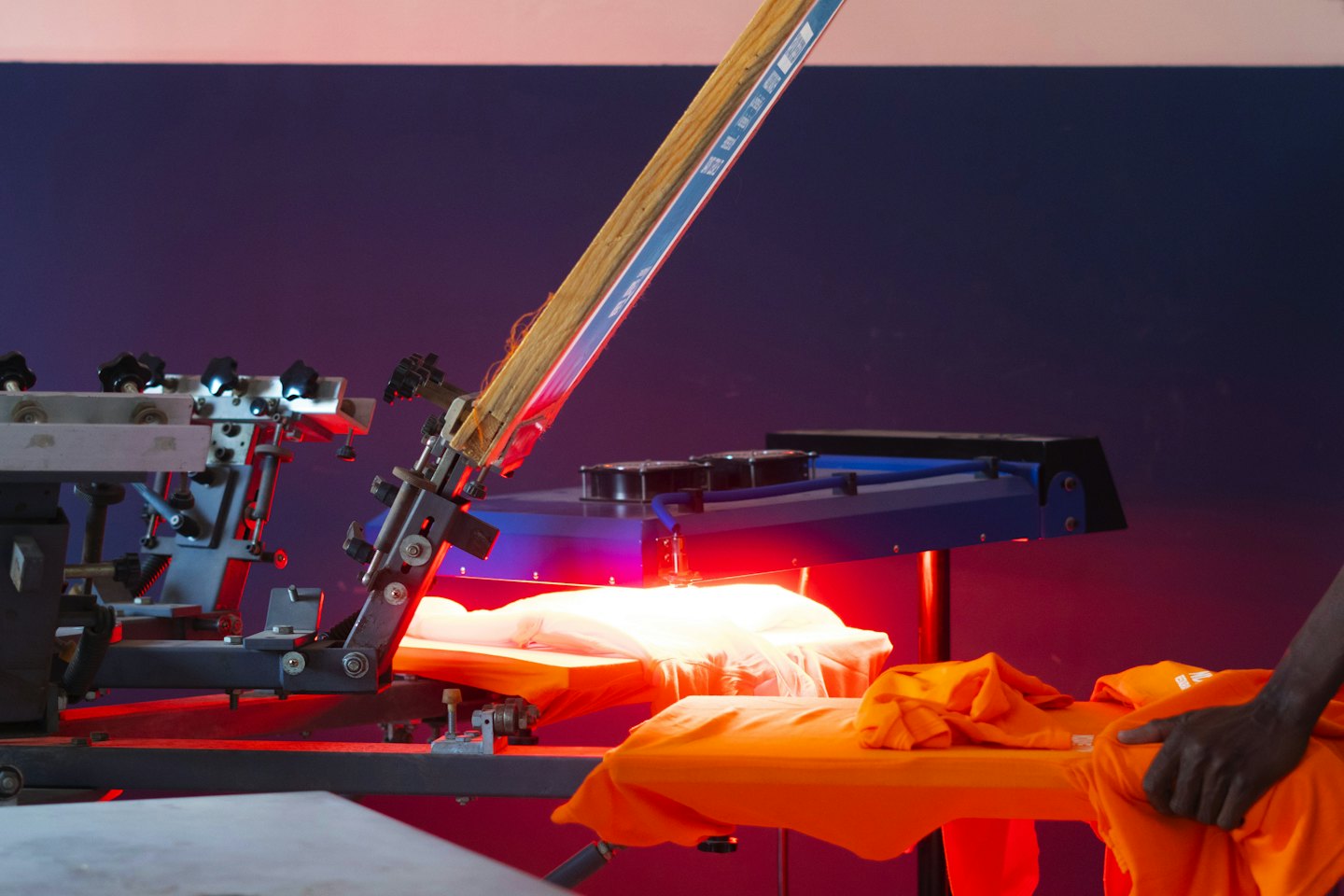 A worker adjusts folded orange shirts near a heat press.