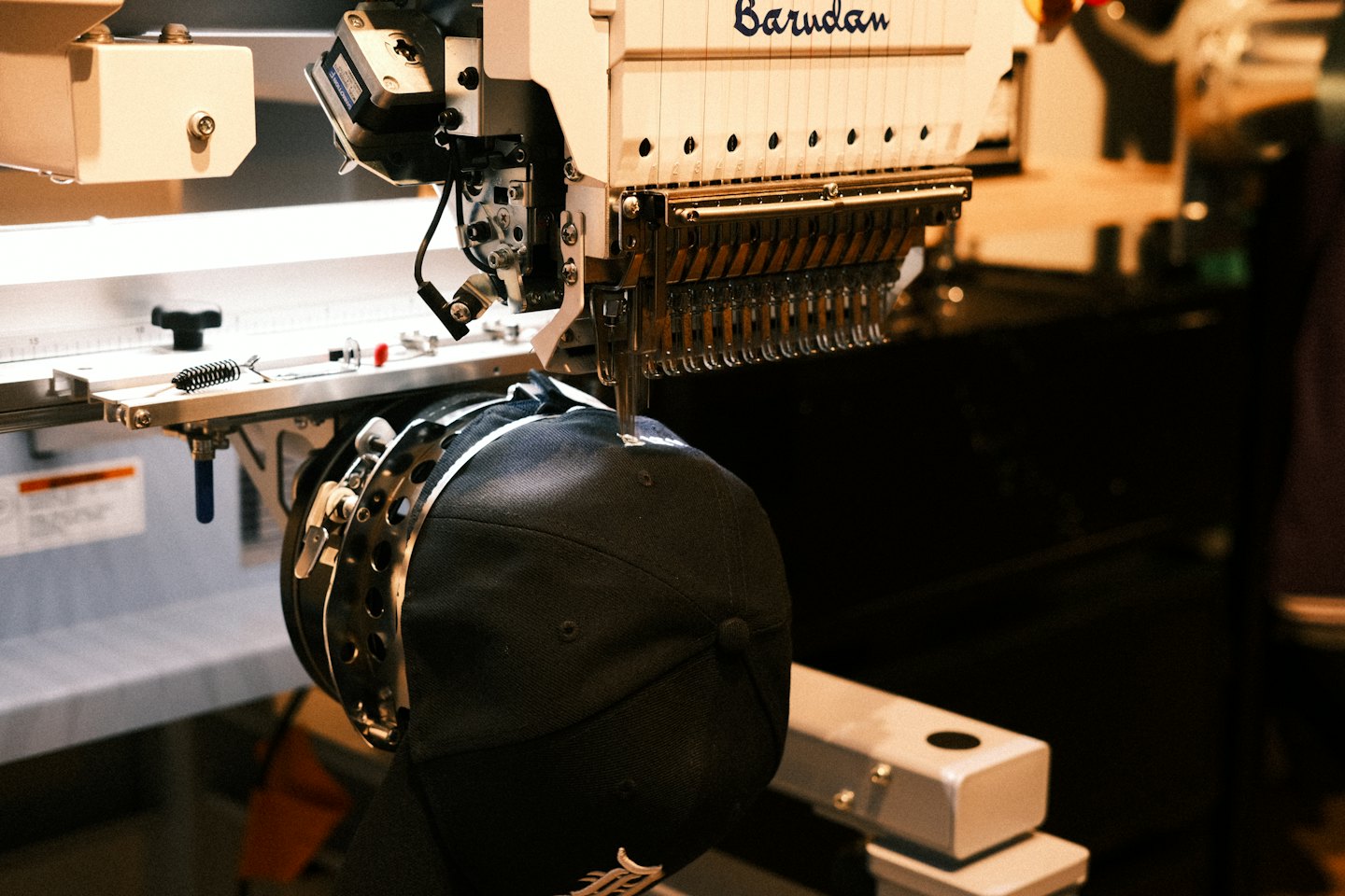 An industrial embroidery machine stitches a design onto a baseball cap.